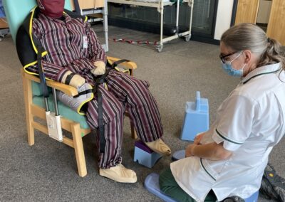 Therapist kneeling, assisting seated individual in care facility - using Patient Handling Training Manikin