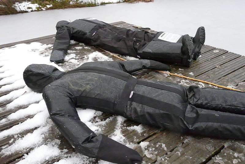 Black manikin immersion suits laid out on snowy dock.