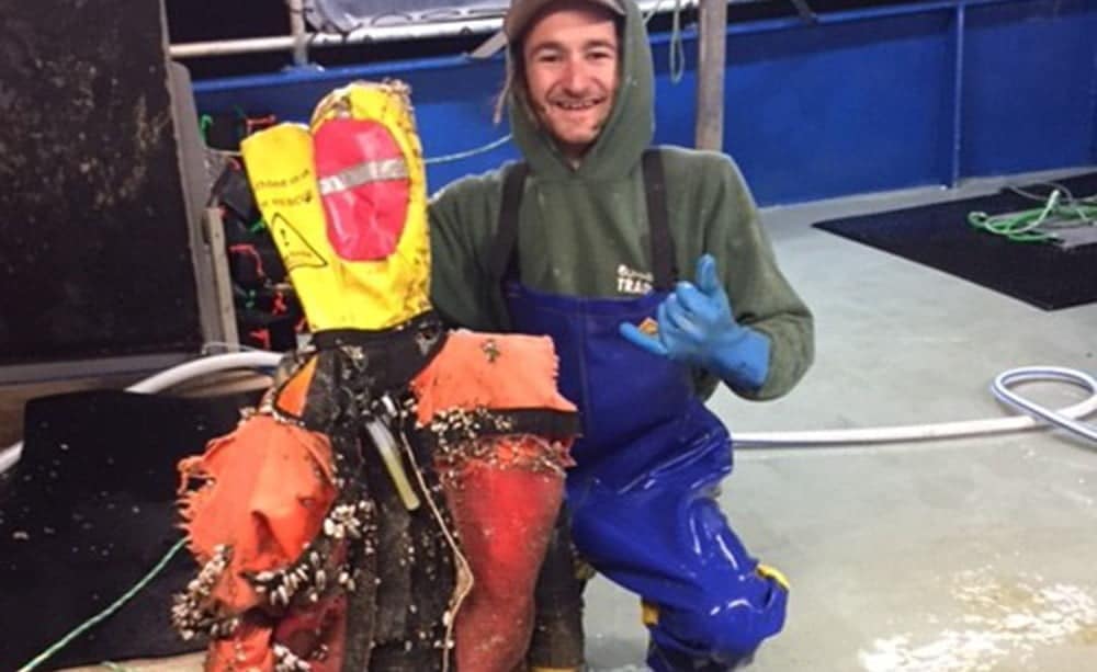 Fisherman posing with sea-bound barnacle-covered manikin.