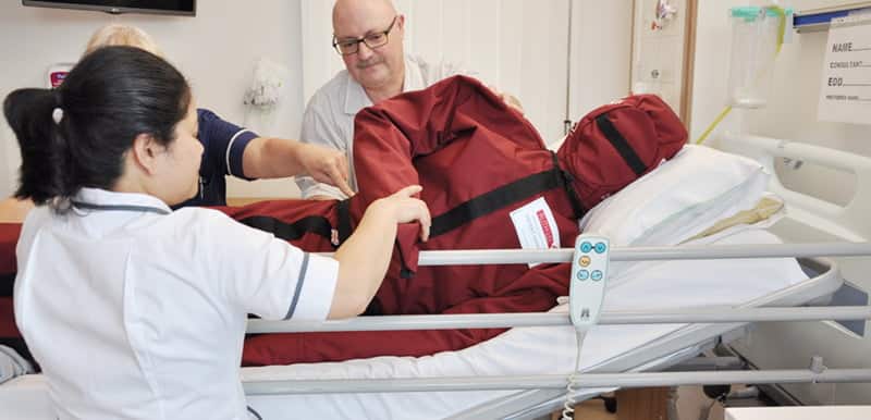 Healthcare workers using patient handling sling in hospital bed.