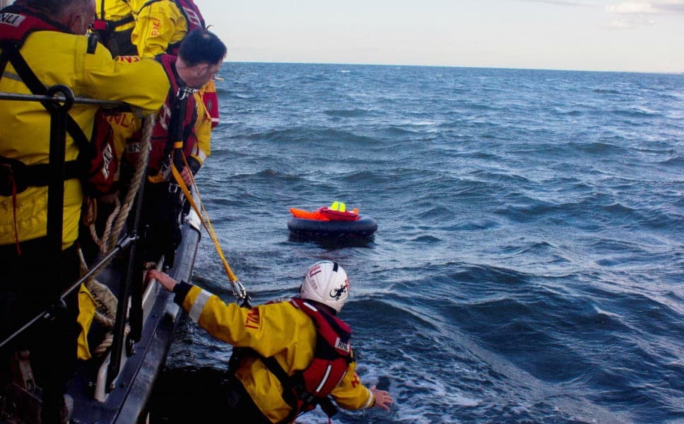 RNLI Rescue team assisting person in water near lifeboat.