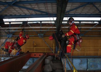 Industrial rescue workers training with ropes indoors.