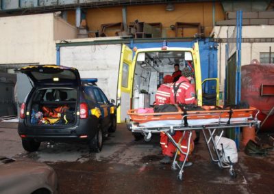 Paramedics loading patient into ambulance at industrial site.