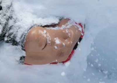 CPR mannequin partially buried in snow.