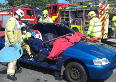 Firefighters rescuing a person from a blue car.