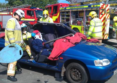 Firefighters rescuing crash victim from blue car.