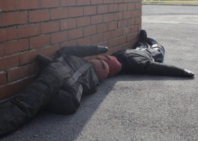 Training dummy lies on pavement next to brick wall.