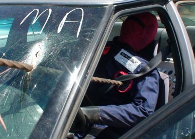 Crash test dummy inside car with damaged windscreen.