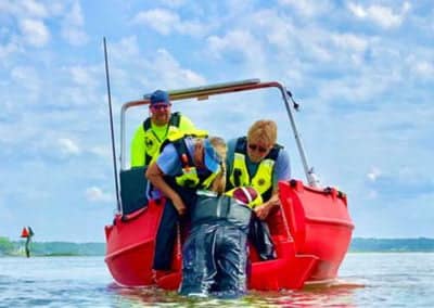 Rescuers assist person into a red lifeboat.