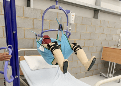 Patient hoist lifting dummy over hospital bed.