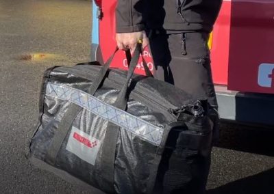 Firefighter carrying black duffel bag near fire truck.