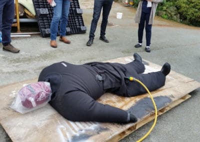 Rescue training dummy on wooden board with people observing.