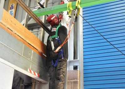 Worker performing safety drill with harness and ladder.