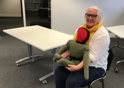 Woman in office holding a green mannequin doll.