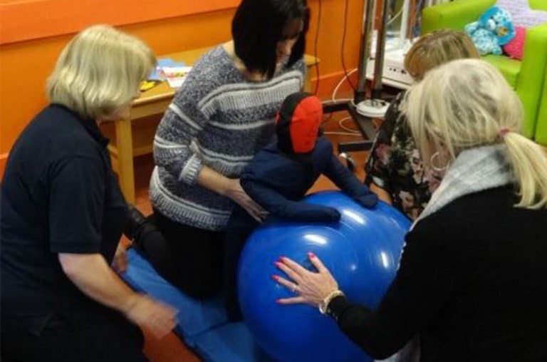 Therapists assisting child on therapy ball in session.