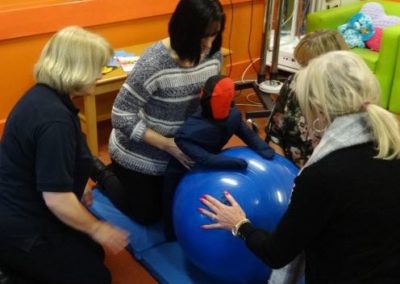 Therapists help child with physiotherapy on exercise ball.