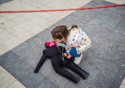 Child practicing first aid on a dummy outside.