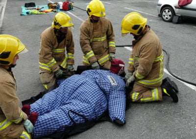 Firefighters practicing rescue techniques on a training dummy.