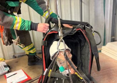 Rescue worker lowering dummy into confined space training area.