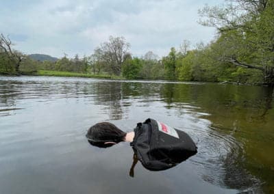 Floating mannequin head in river surrounded by trees.