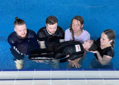 Adults practising water rescue techniques in a swimming pool.