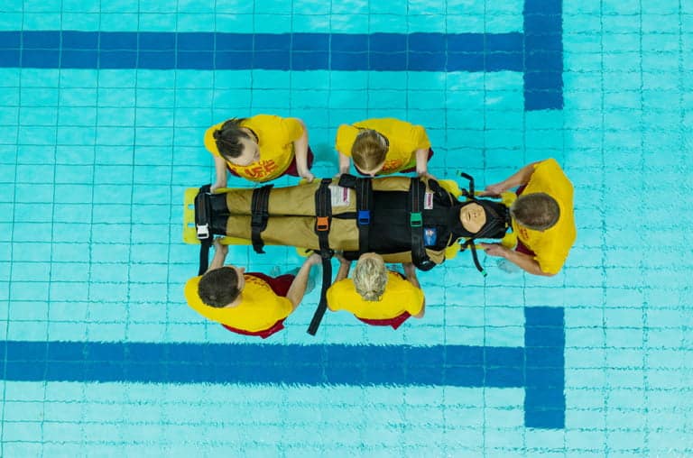 Four lifeguards practising poolside rescue with training mannequin.