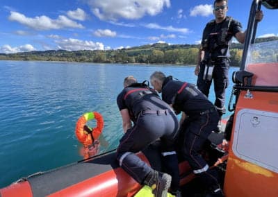 Rescue team on boat assisting a person rescue manikin in water.