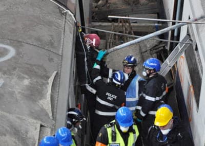 Rescue workers aiding trapped person in train wreckage.