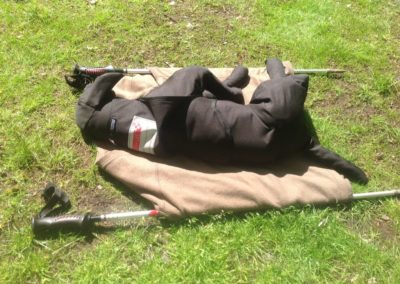 Sleepy dog wrapped in coat, lying on grass.