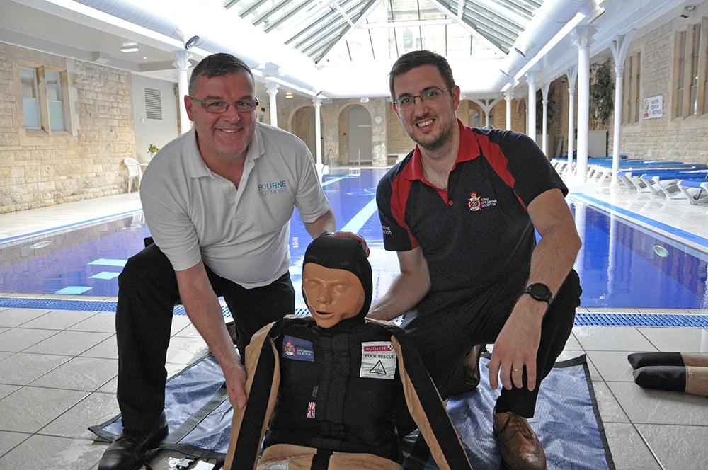 Two men practising poolside rescue with training dummy.