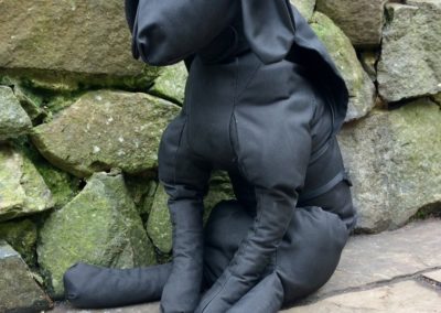Black fabric dog sculpture against a stone wall.