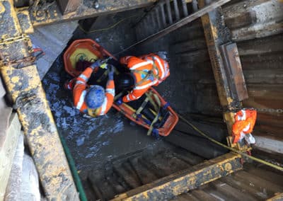 Rescue workers assisting person in flooded construction site.