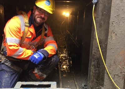 Construction worker in muddy underground site with safety gear.