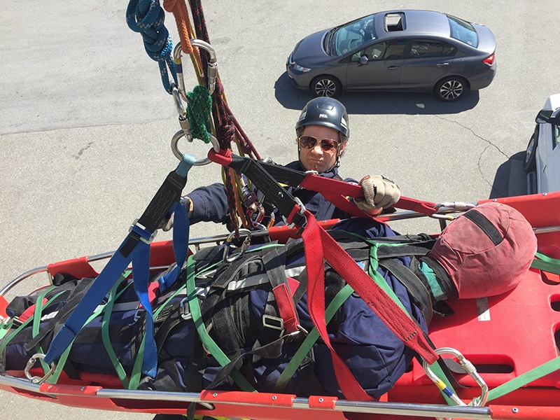 Rescue worker securing person in stretcher during emergency drill.