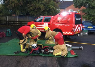 Firefighters preparing equipment next to red response vehicle.