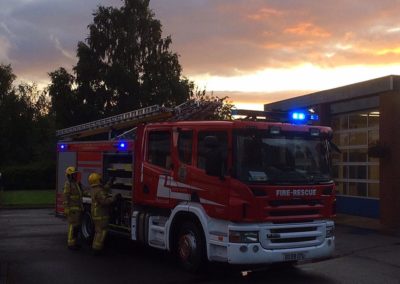 Fire engine outside station at sunset with firefighters.