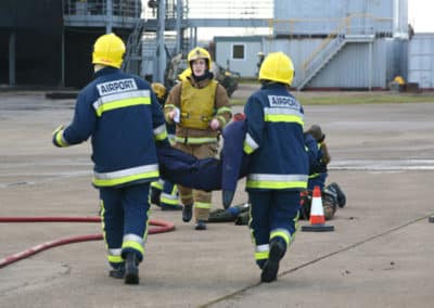 Airport firefighters carrying injured person during training exercise.