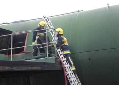 Firefighters working on a ladder near a green structure.