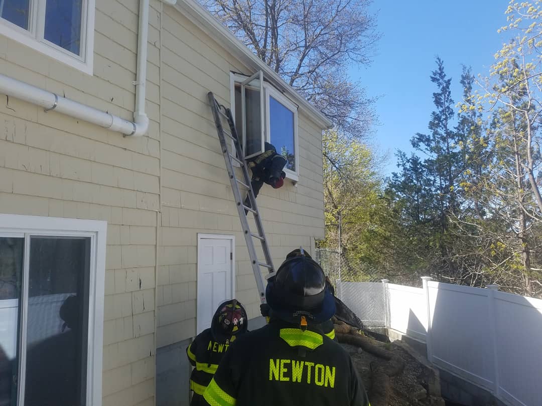 Firefighters rescuing person through window with ladder.