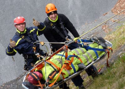 Rescue team carrying a stretcher down a steep slope.