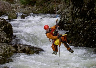 Rescue worker suspended above raging river rapids.