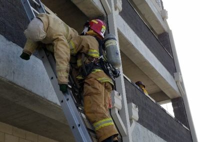 Firefighter conducting rescue drill on a building ladder.