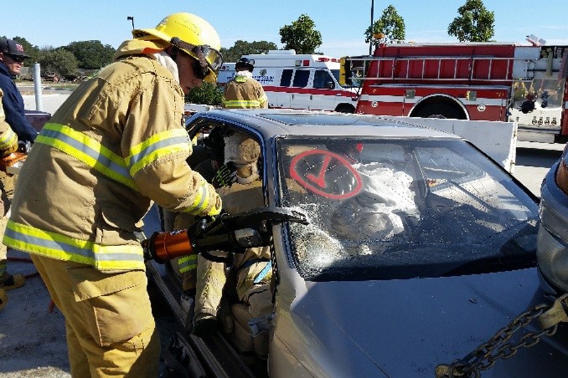 Firefighters using rescue equipment on a crashed car.