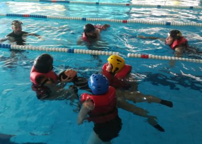Swimming pool rescue training session with helmets and life jackets.