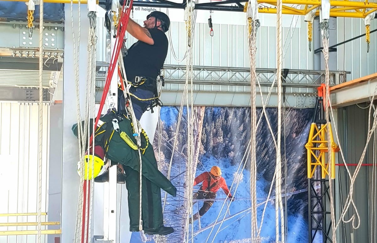 Workers practising industrial rope access techniques indoors.