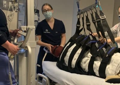 Medical staff using hoist to lift patient in hospital.