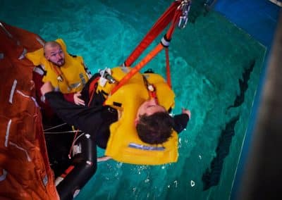 Two people practice lifeboat rescue in pool.