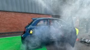 Car emitting smoke near building with open door.